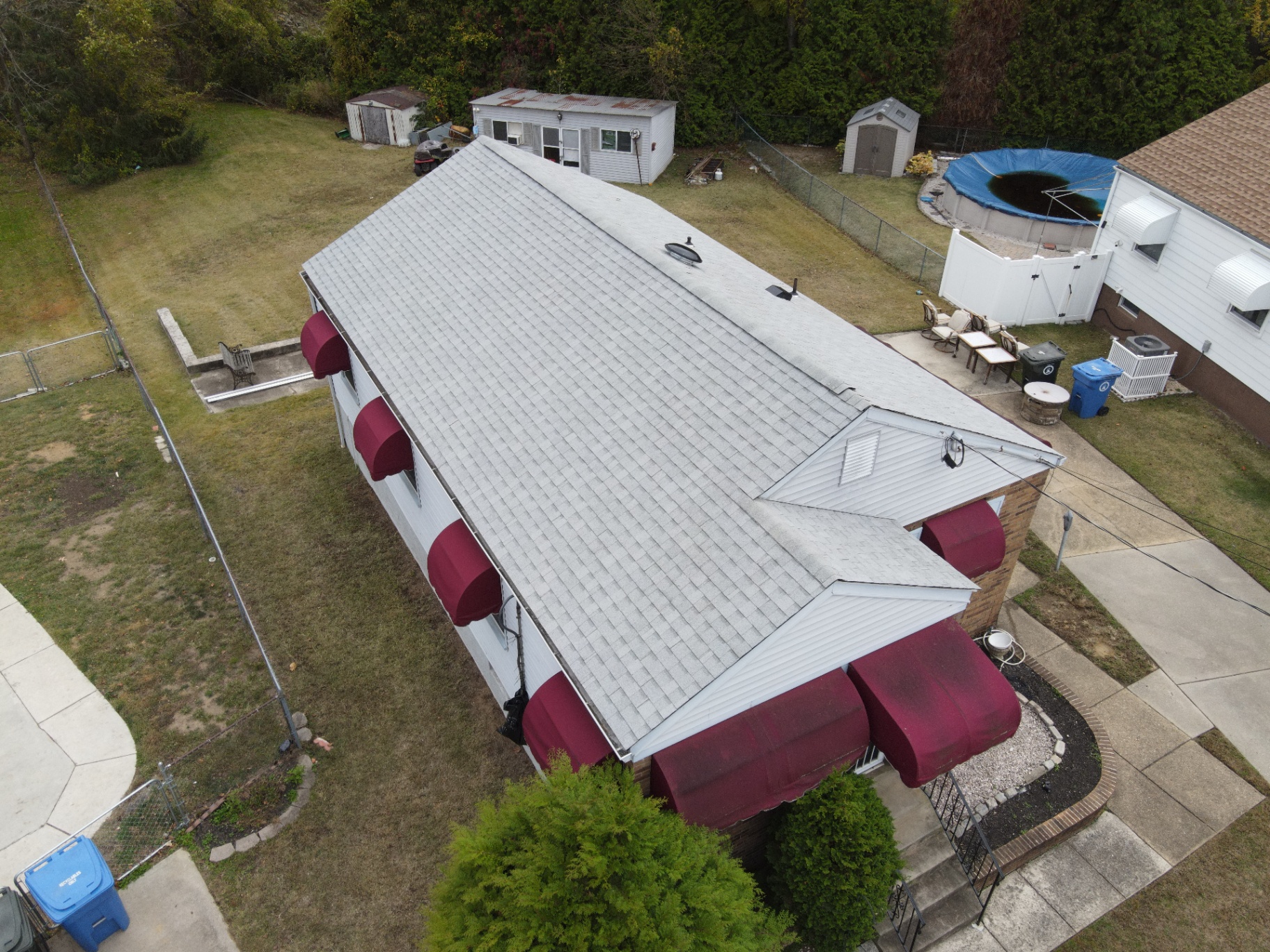 Completed pale-gray shingle roof on a long residential structure with burgundy awnings
