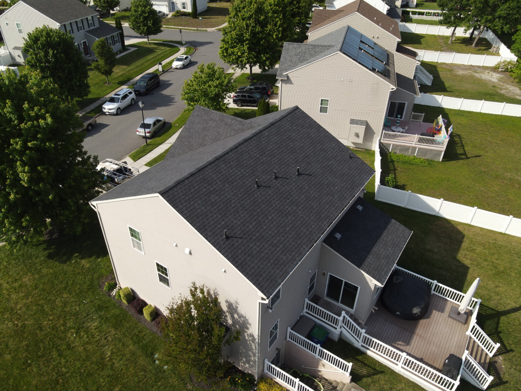Completed black shingle roof on a two-story home with white fence
