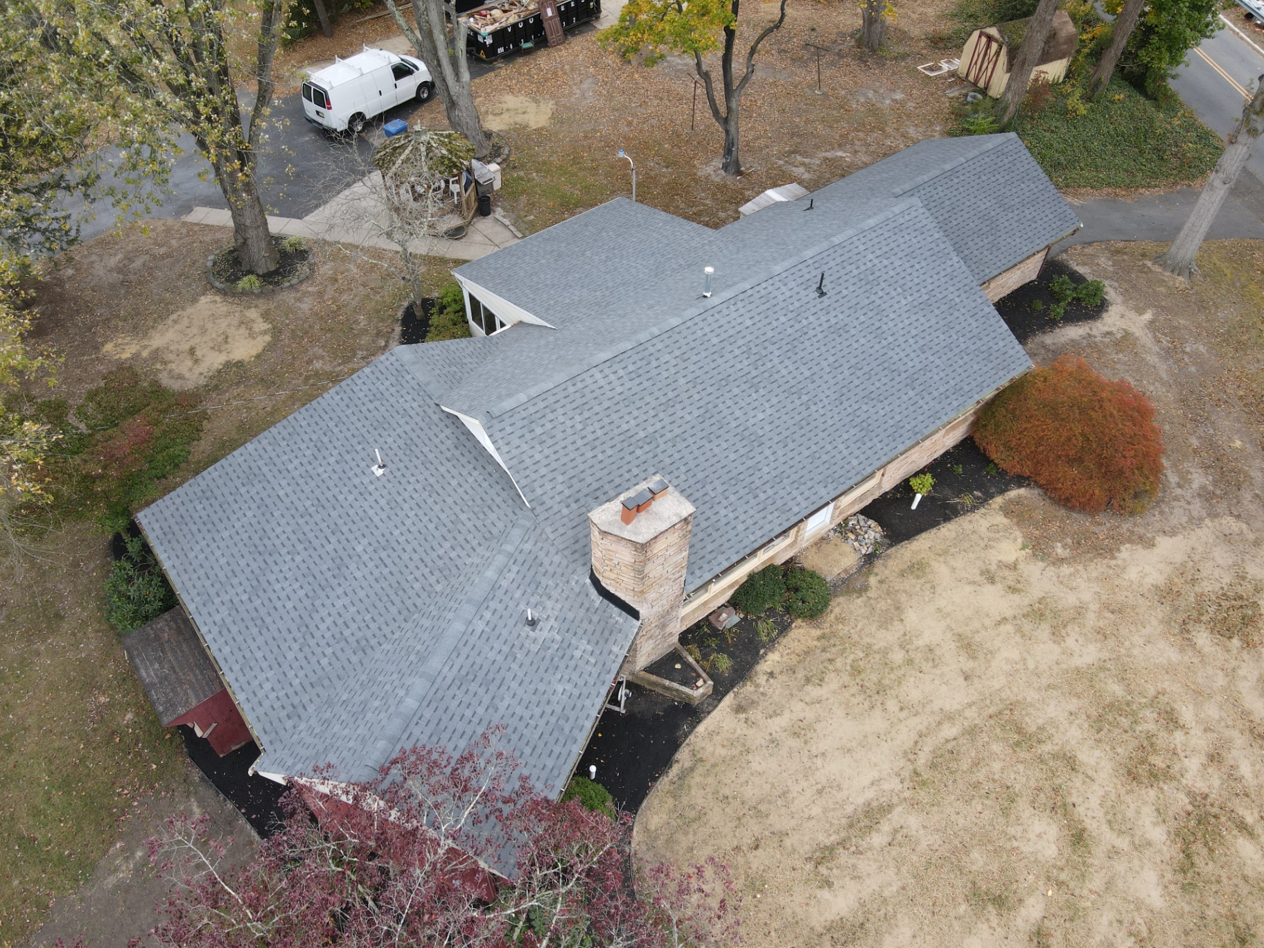 Aerial before photo of a ranch home with worn brown shingles and a tan stone chimney
