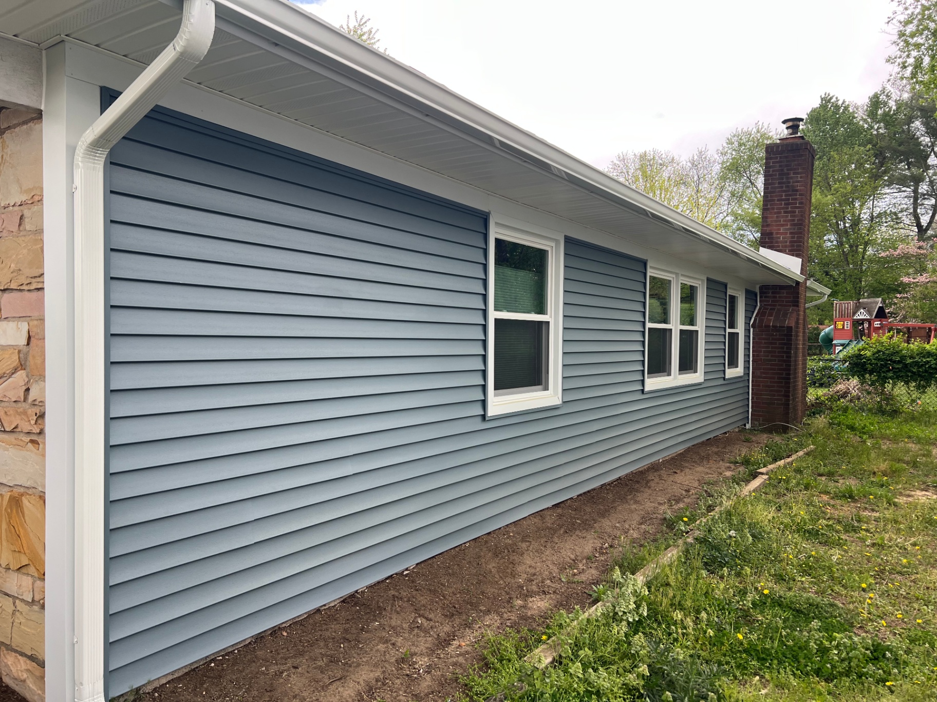 Side wall of a ranch home with new blue-gray vinyl siding and white trim