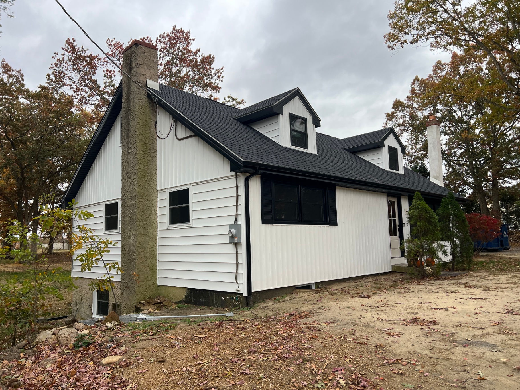 Side and rear of a cape home with white vinyl siding, dormers and black trim