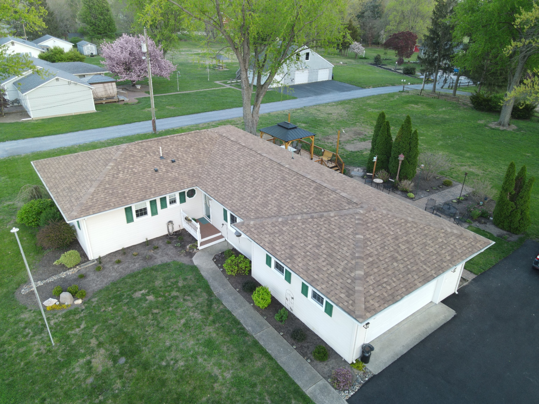 Completed tan shingle roof on a long ranch home with green shutters